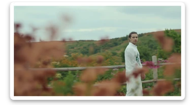 A portrait of a white person in the foreground, blurred plants in the foreground, a wooden fence and colorfull flowers in the midground, rolling hills in the background, cinematic depth of field, layered composition, natural lighting sticker