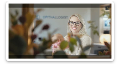 Cinematic still, blurred plants in the foreground (frame within a frame), Proffesional advertising of a smiling european white woman with glasses smiling holding baby, minimalistic ophthalmologist interior in background, leading  lines, "rule of thirds", 60/30/10 colors, soft light, warm colors sticker