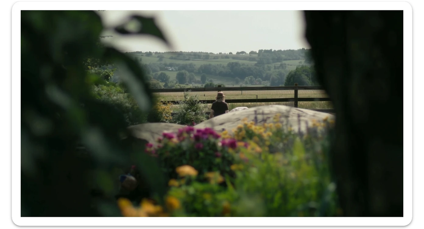 "Two shot" of a person in the foreground, blurred plants in the foreground (frame within a frame), a wooden fence and colorfull flowers in the midground, Poland, rolling hills in the background, cinematic depth of field, layered composition, natural lighting sticker