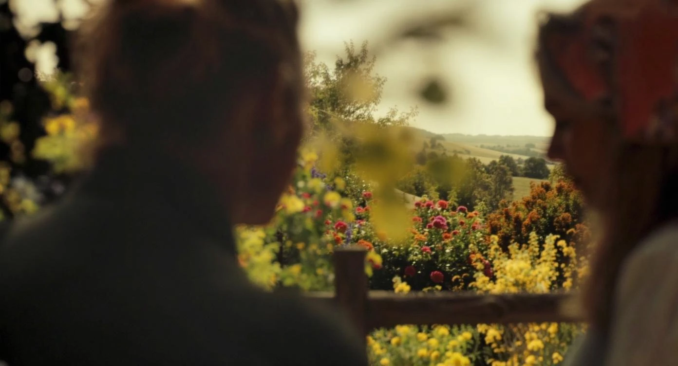 "Two shot" in the foreground, blurred plants in the foreground (frame within a frame), a wooden fence and colorfull flowers in the midground, Poland, rolling hills in the background, cinematic depth of field, layered composition, natural lighting emoji