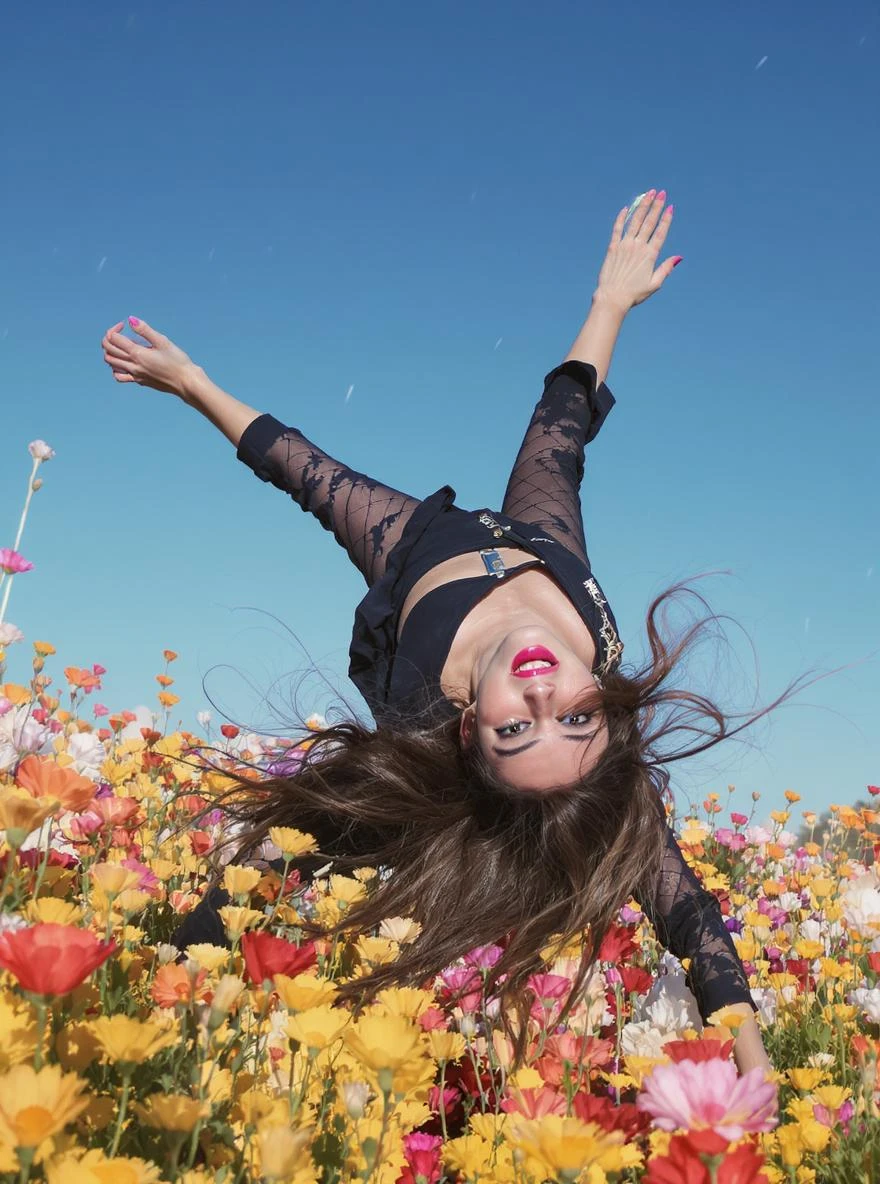Closeup photo of a woman falling down (almost hit the ground) around colorfull flowers wearing alternative fashion, blue sky minimalistic background emoji
