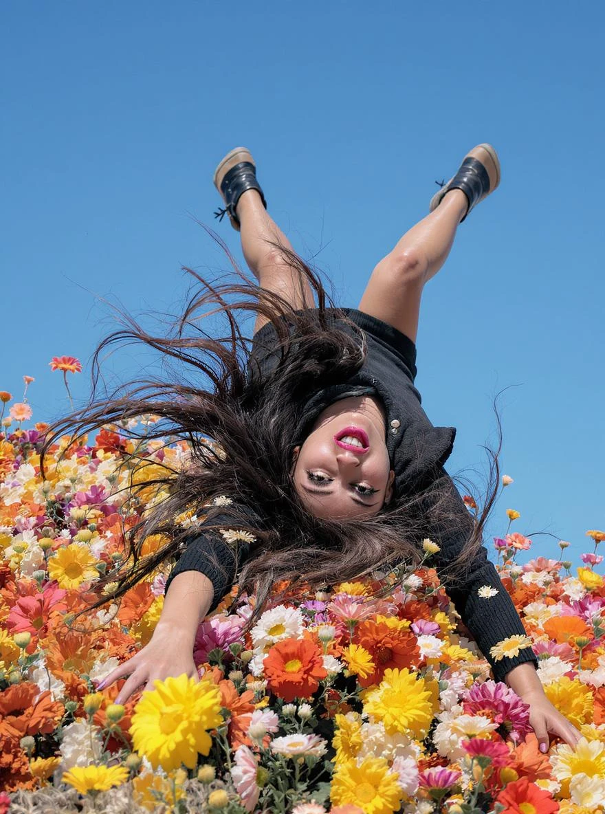 Closeup photo of a woman falling down (almost hit the ground) around colorfull flowers wearing alternative fashion, blue sky minimalistic background emoji