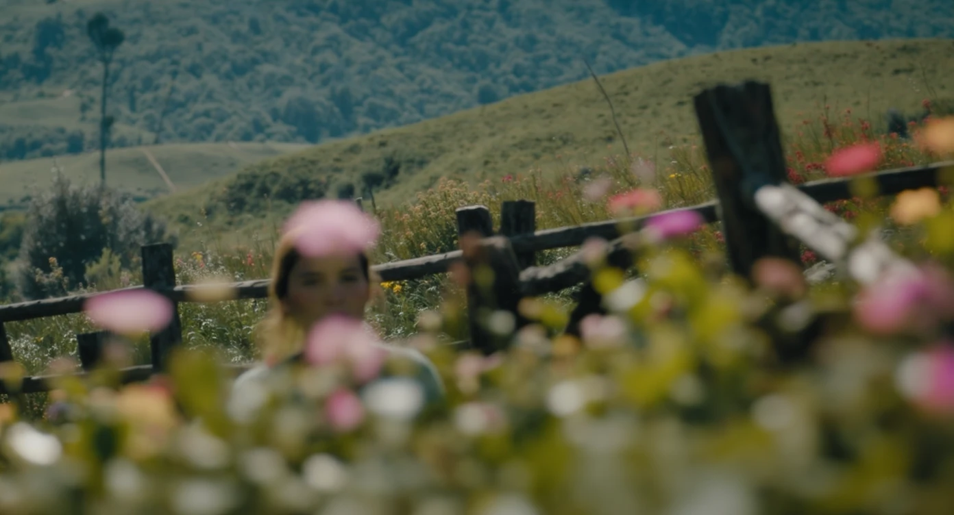 A portrait of a person in the foreground, blurred plants in the foreground (close to the camera), a wooden fence and colorfull flowers in the midground, rolling hills in the background, cinematic depth of field, layered composition, natural lighting emoji