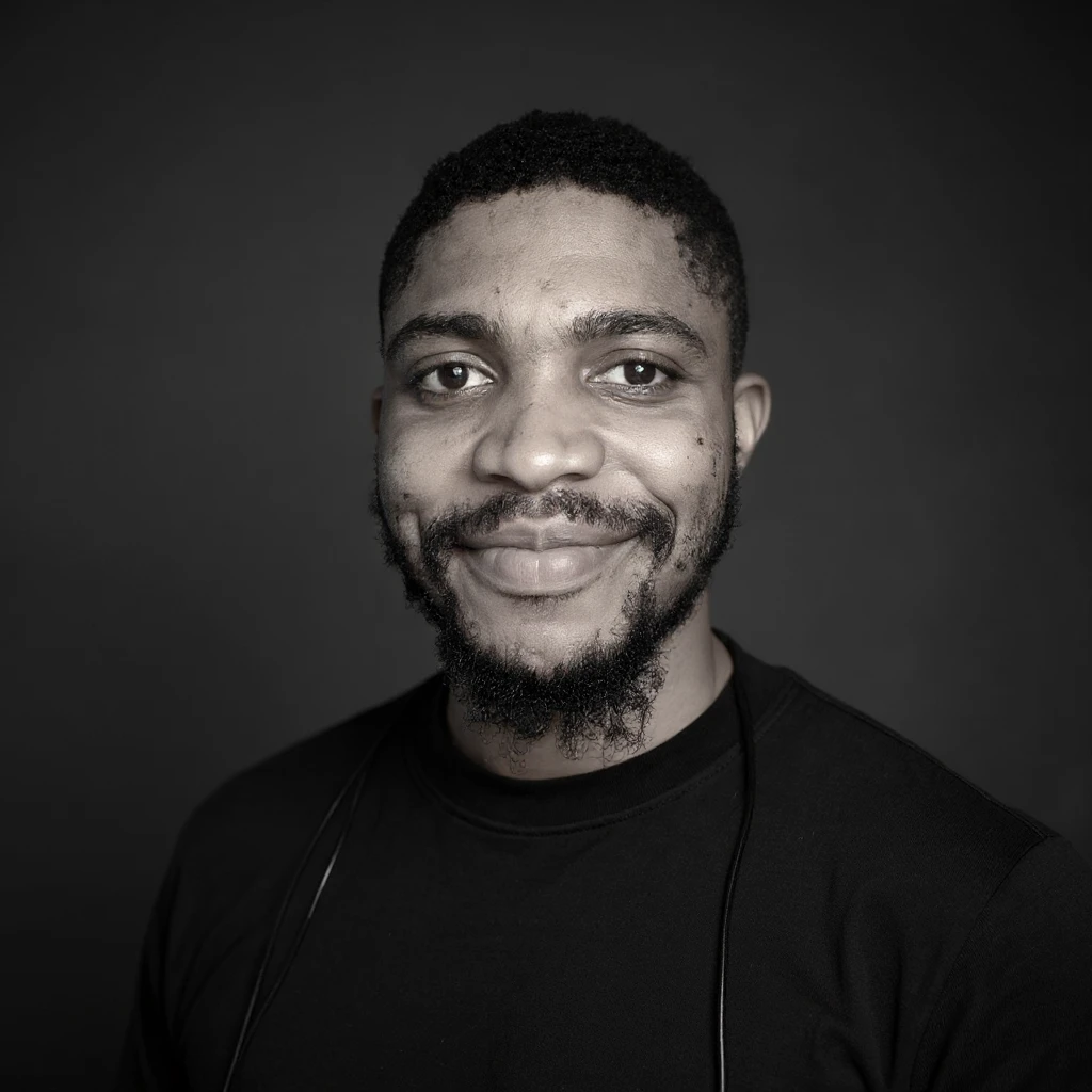 A professional portrait of me in monochrome. Plain black crew neck shirt. Tailored to LinkedIn. Tech boy vibe (programmer). I’m a black man from Nigeria. Retain facial features from attached image. Smooth skin. No accessories. emoji