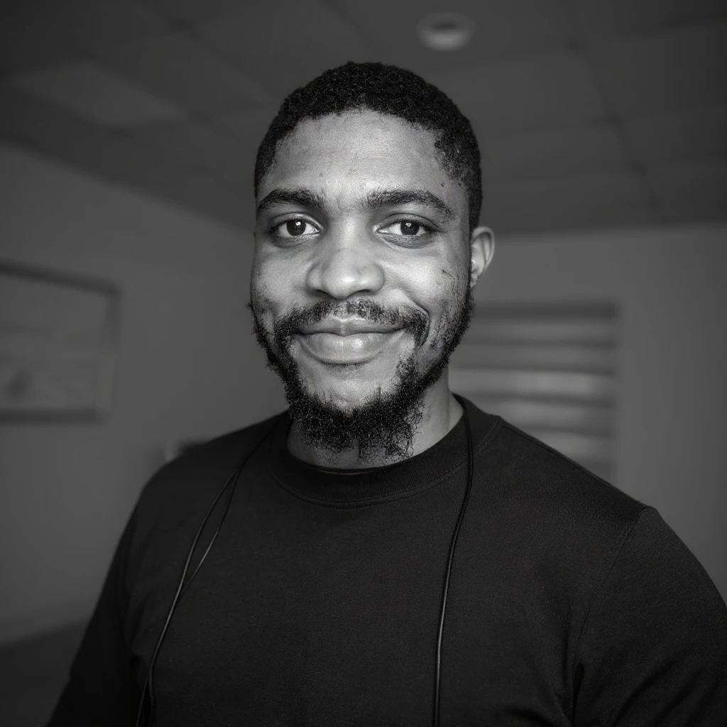 A professional portrait of me in monochrome. Plain black crew neck shirt. Tailored to LinkedIn. Tech boy vibe (programmer). I’m a black man from Nigeria. Retain facial features from attached image. Smooth skin. No accessories. emoji