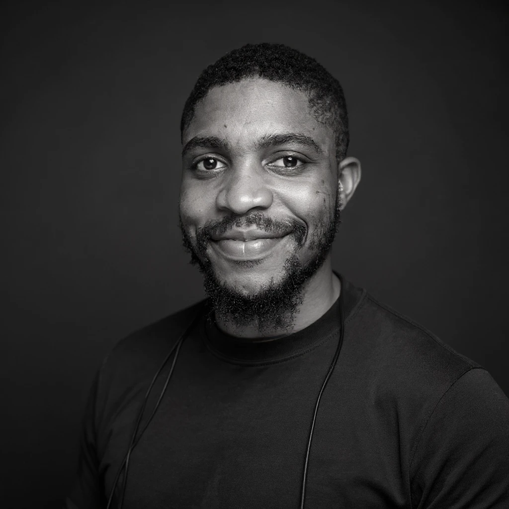 A professional portrait of me in monochrome. Plain black crew neck shirt. Tailored to LinkedIn. Tech boy vibe (programmer). I’m a black man from Nigeria. Retain facial features from attached image. emoji