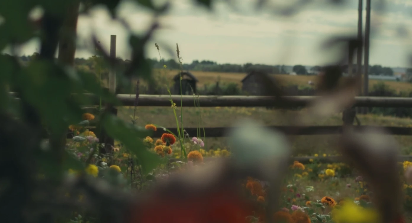 A portrait of a person in the foreground, blurred plants in the foreground (frame within a frame), a wooden fence and colorfull flowers in the midground, Poland, rolling hills in the background, cinematic depth of field, layered composition, natural lighting emoji